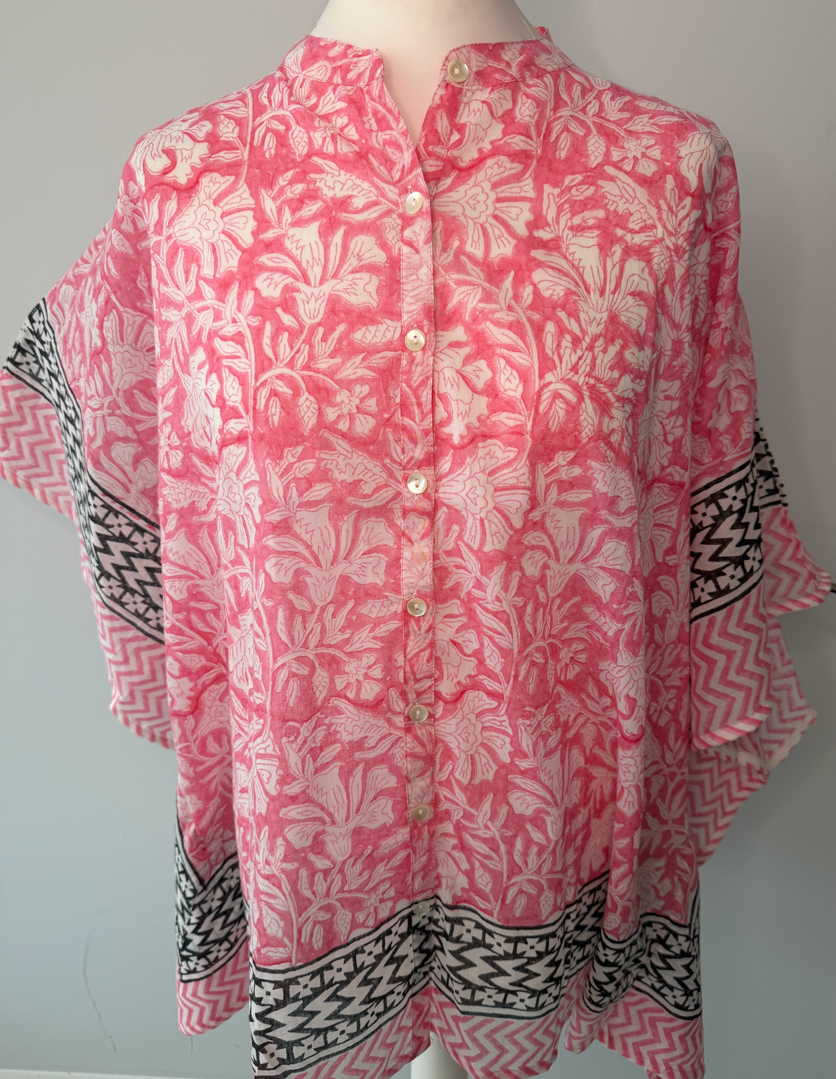 A pink and white floral print button-up blouse with black and white patterned borders on the sleeves and hem, displayed on a mannequin torso.