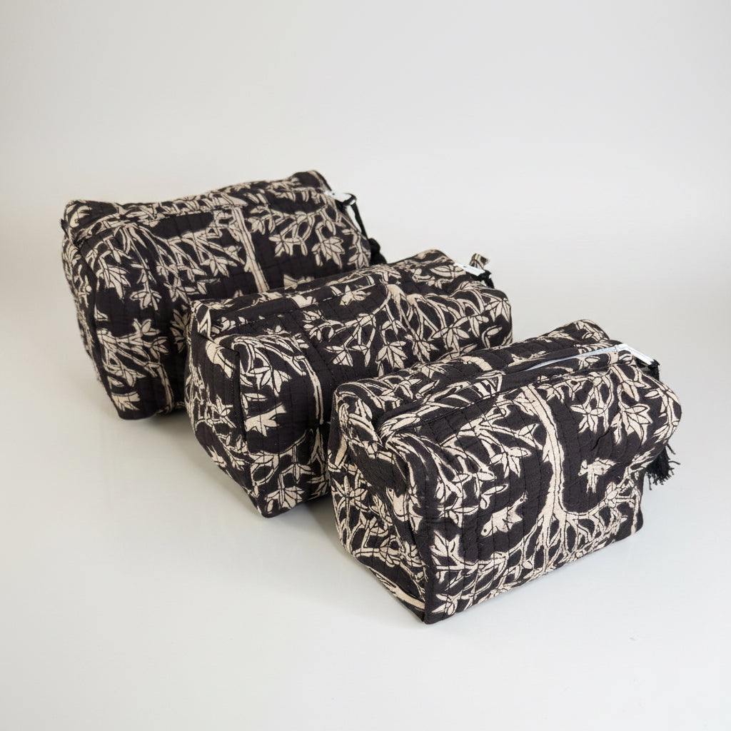 Three quilted cosmetic pouches in a black and beige botanical branch pattern, arranged diagonally on a light-colored marble surface.