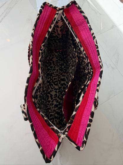 A top-down view of a quilted handbag with a leopard print exterior, bright pink quilted side panels, and a leopard print interior lining, resting on a white marble surface.