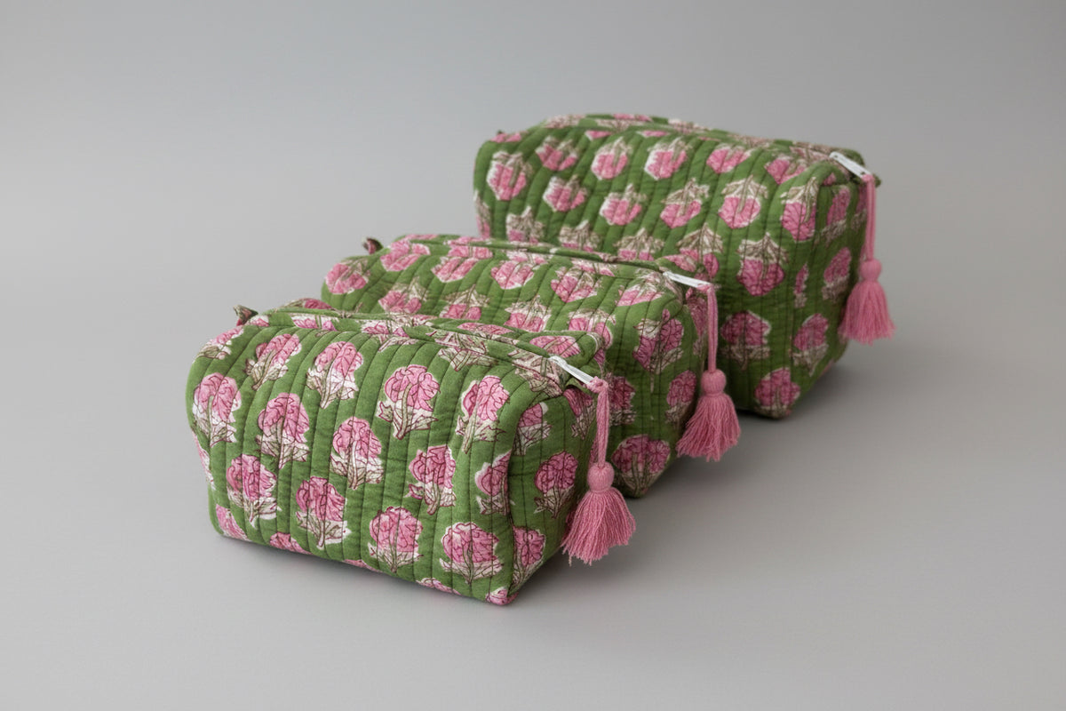 Three quilted cosmetic pouches with a green and pink floral pattern, stacked on a white marble surface.