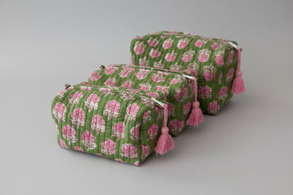 Three quilted cosmetic pouches with a green and pink floral pattern, stacked on a white marble surface.